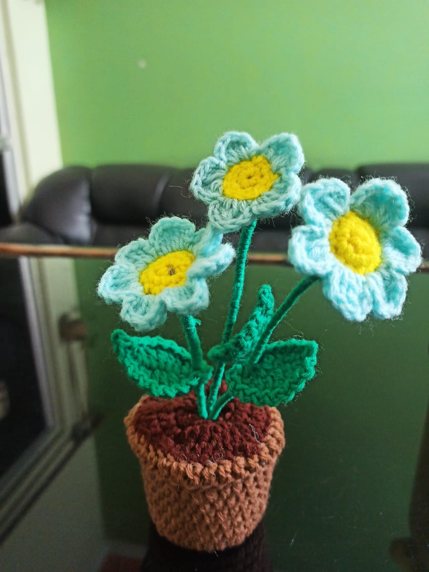 Crocheted potted plant with blue daisy flowers, made by a woman beneficiary