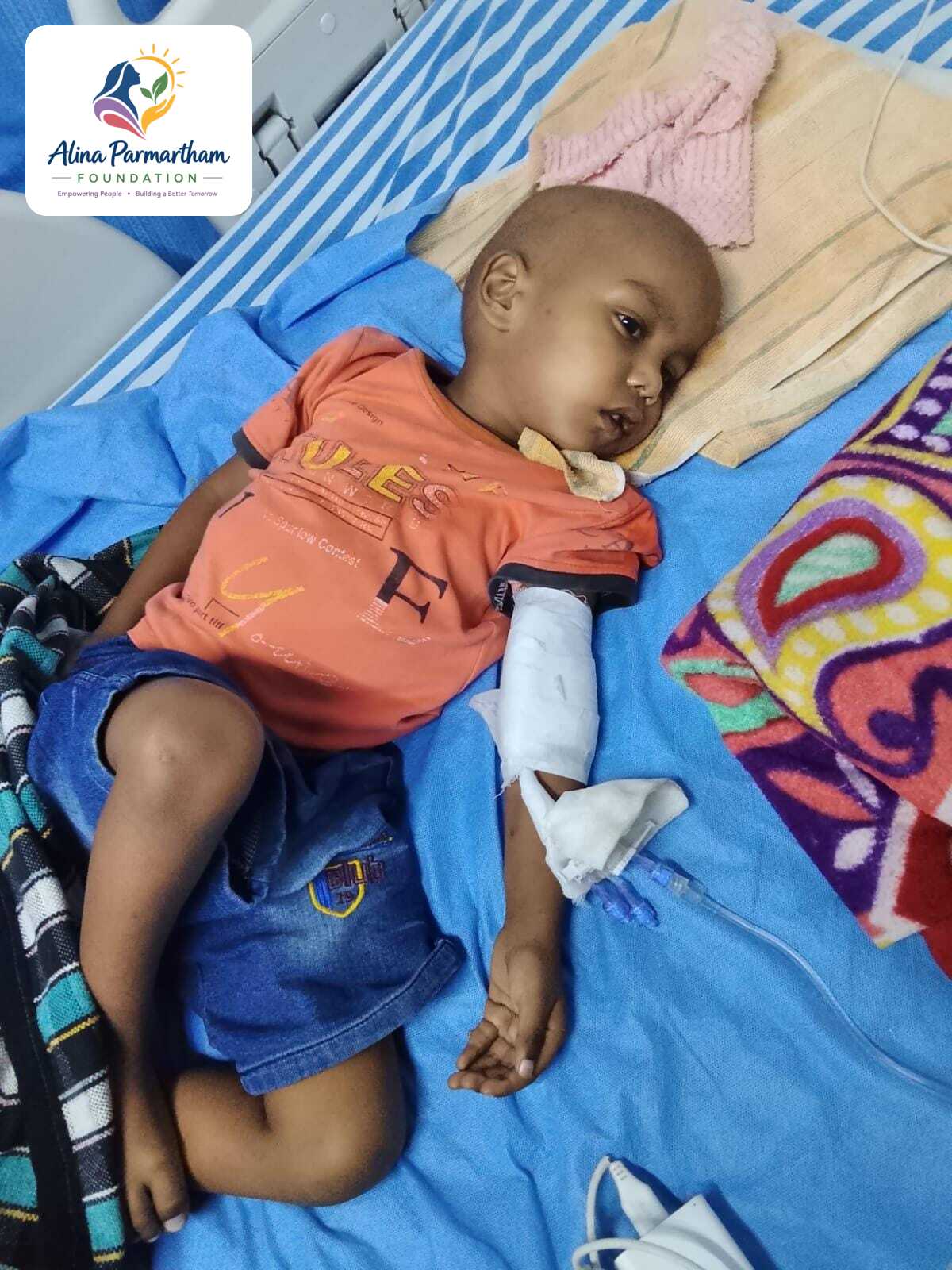 Shrikant, 3 years old, resting in a hospital bed during his blood cancer treatment, with the Alina Parmartham Foundation logo