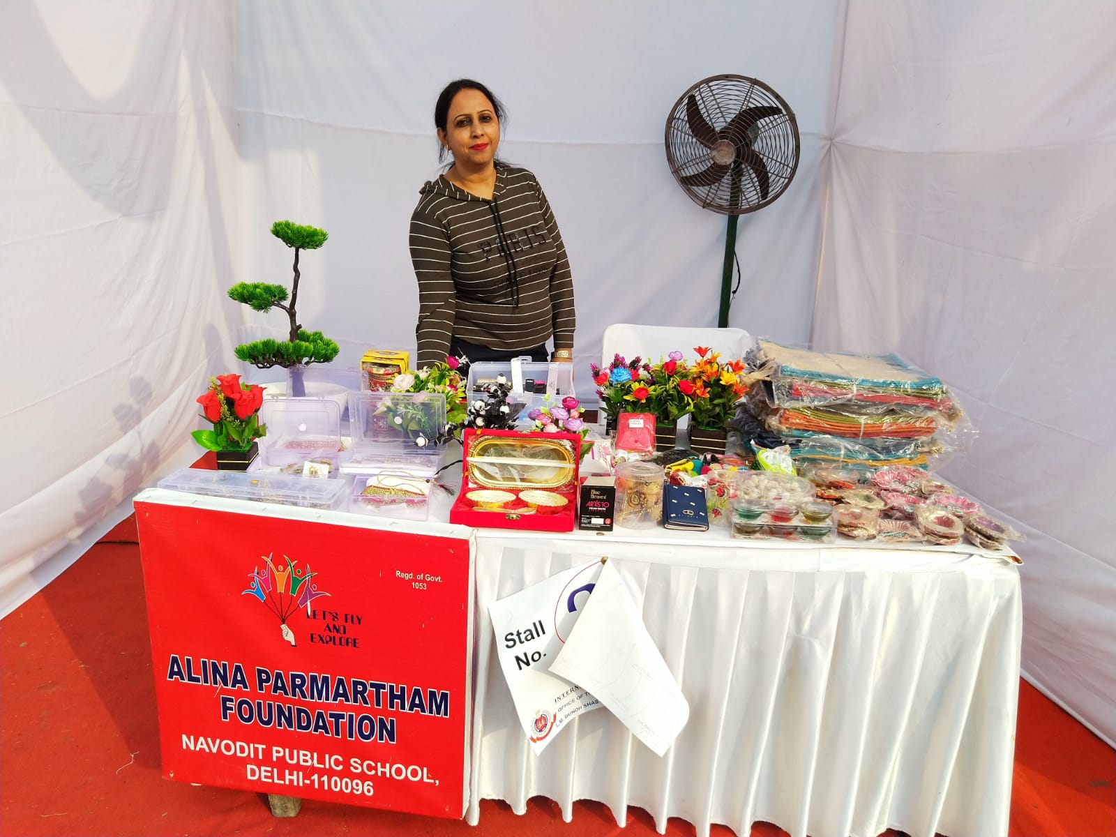 Woman behind an Alina Parmartham Foundation exhibition stall displaying gift boxes, décor and accessories